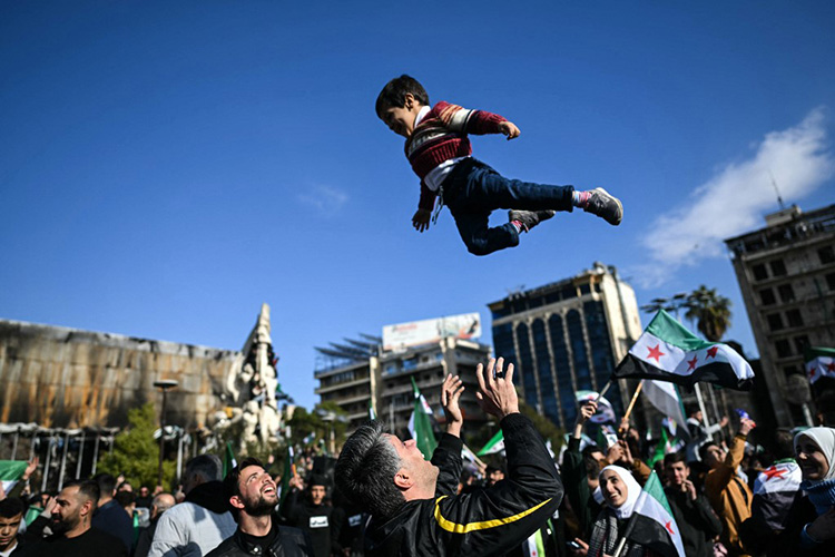 Un homme lance joyeusement un garçon en l'air au moment où des gens se rassemblent après la prière du vendredi, pour célébrer le renversement du président Bashar al-Assad à Alep, le 13 décembre 2024. © Ozan Kose / AFP